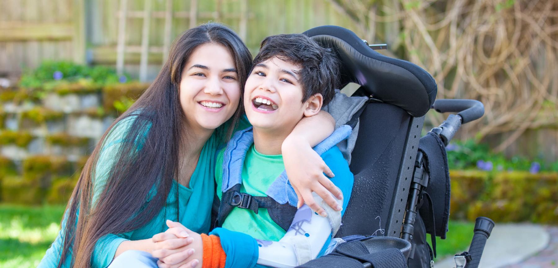 Teenage girl hugging disabled brother in wheelchair outdoors